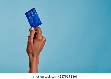 Close up of african woman hand holding bank credit card to make a payment with copy space. Black woman hand holding credit card for financial transaction or contact less payment isolated on blue wall. - Powered by Shutterstock