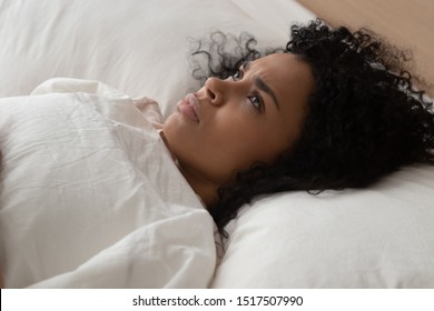 Close Up African Woman Lying In Bed Having Sleep Disorder Sleeping Trouble Looking At Ceiling Cannot Fall Asleep Suffers From Insomnia Caused By Anxiety, Stress, Depression Or Noisy Neighbours Concept