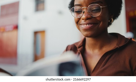 Close Up African Woman In A Relaxed Mood Reading Interesting Book Outdoors, Wearing Glasses. Happy Expression