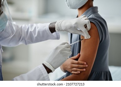 Close up of African-American girl getting vaccinated in child vaccination clinic with doctor injecting syringe needle in shoulder, copy space