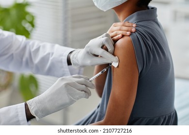 Close up of African-American girl getting vaccinated in child vaccination clinic with focus on doctor injecting syringe needle in shoulder, copy space - Powered by Shutterstock