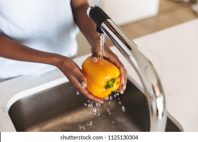 Close up of a afro american woman washing capsicum to make a salad at the kitchen - Powered by Shutterstock