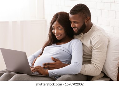 Close up of afro pregnant couple using laptop at home, man hugging his wife tummy, free space