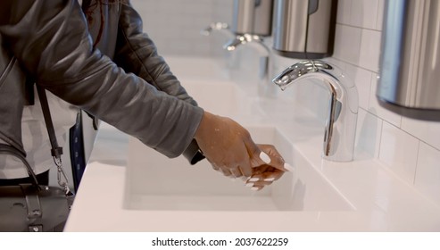 Close Up Of Afro-american Woman In Mask Washing Hands With Soap In Bathroom In Public Place. African Young Female Clean Hands In Sink At Public Restroom