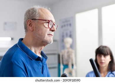 Close Up Of Aged Patient Using Gear For Physical Exercise And Recovery After Accident. Man With Muscle Pain Doing Sport Workout And Stretching To Recover With Assistance From Nurse