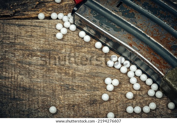 Close up of airsoft gun magazine and airsoft\
balls on wooden\
background