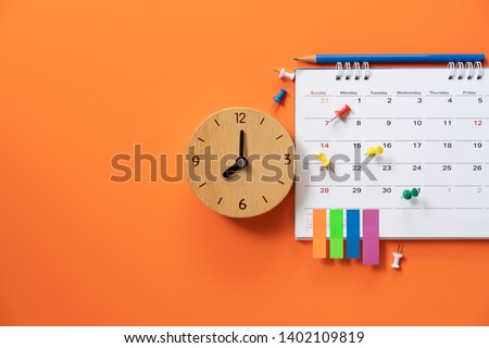 close up of alarm clock and calendar on the orange table background, planning for business meeting or travel planning concept