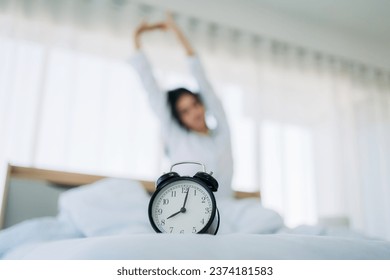 Close up of alarm clock on bedside table. Young Woman Waking Up with Happiness in Cozy Bedroom at Home. Beautiful Girl Smiling and Relaxing in Bed after Waking Up.
