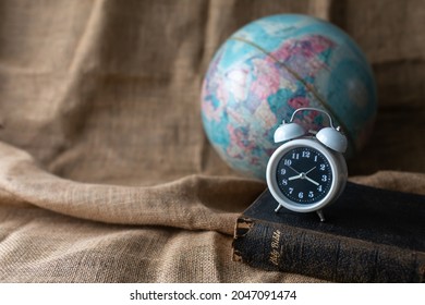Close up of alarm clock on the old holy bible with blurred world globe on vintage linen sackcloth background against, copy space, Christian background, bible study or the world end time concept.