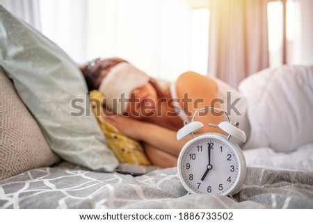 Close up alarm clock and peaceful woman sleeping on background under warm blanket in comfortable bed, young female resting in bedroom, enjoying dreams