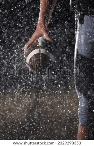 Close up of American Football Athlete Warrior Standing on a Field focus on his Helmet and Ready to Play. Player Preparing to Run, Attack and Score Touchdown. Rainy Night with Dramatic lens flare