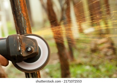Close up of an angle grinder machine in motion, removing rust from an old metal construction outdoors with sparks flying. Shallow depth of field