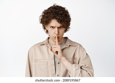 Close Up Of Angry Curly Man Shushing, Making Shut Up Shush Gesture And Staring Threatening, White Background