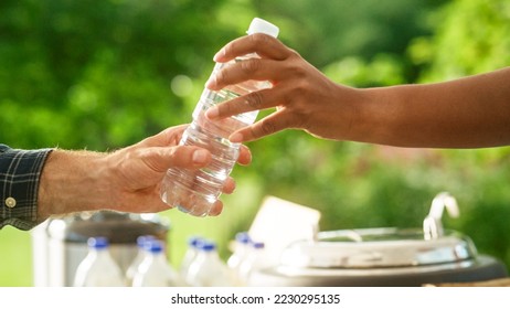 Close Up of a Anonymous Person Handing Over a Water Bottle to Another Person. Green Background in Nature. Outdoors Fourt Court Selling Drinks. Ecology, Healthcare and Hydration Concept.