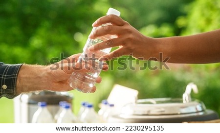 Close Up of a Anonymous Person Handing Over a Water Bottle to Another Person. Green Background in Nature. Outdoors Fourt Court Selling Drinks. Ecology, Healthcare and Hydration Concept.