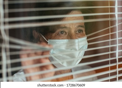 Close up of anxious old woman surgical mask looking through window blinds during self-quarantine. Senior female wearing face mask looking outside the window at hospital. - Powered by Shutterstock