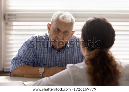 Close up anxious serious old man listening to female doctor at meeting in hospital, therapist physician consulting mature patient about disease, treatment, elderly generation healthcare concept