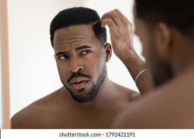 Close up anxious unhappy African American man checking hair after shower, looking in mirror, standing in bathroom at home, dissatisfied by hair loss or dandruff, healthcare and beauty concept
