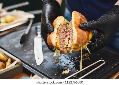 Close up of appetising beef burger. Chef's hands divide into half cooked hamburgers from beef. Street food ready to serve on a food stall. Chef cooks an American tasty hamburger. - Powered by Shutterstock