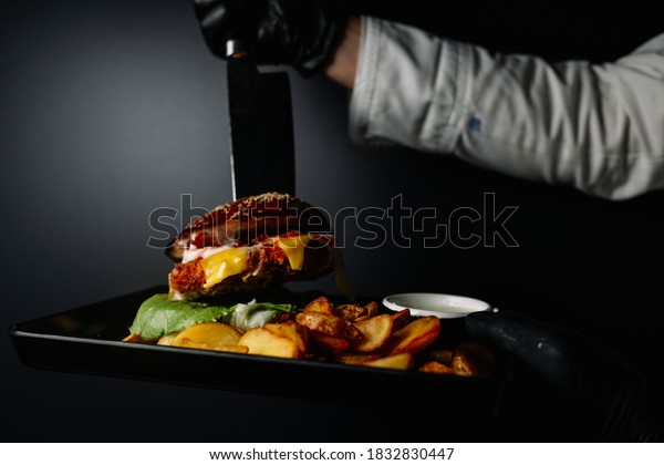 Close up of\
appetising beef burger. Chef\'s hands divide into half cooked\
hamburgers from beef. Street food ready to serve on a food stall.\
Chef cooks an American tasty\
hamburger.