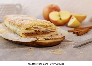 close up of an apple pastry strudel roll with cinnamon on grey marble table, apples in background. Thanksgiving desert meal. High quality photo