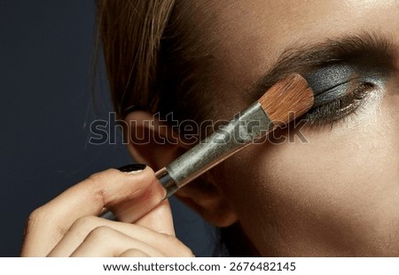 Close up applying dark eyeshadow with makeup brush on eyelid