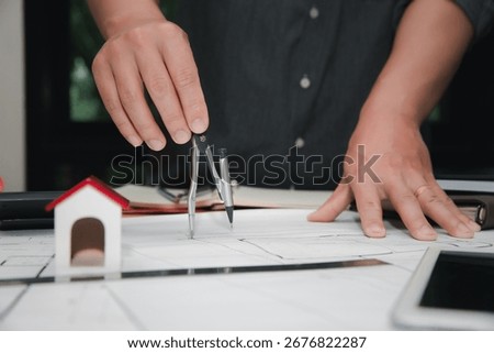 Close up of architect hand using compass drawing house plan on blueprint, architecture and construction concept.