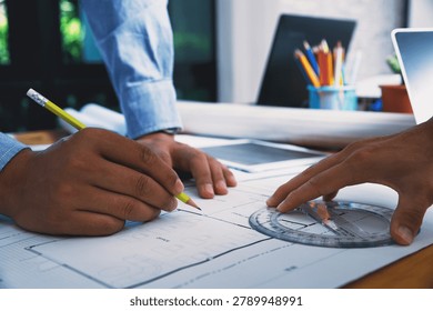 Close up of architect hand using pencil and protractor to draw architectural building plan on blueprint paper at desk.