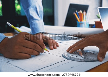 Close up of architect hand using pencil and protractor to draw architectural building plan on blueprint paper at desk.