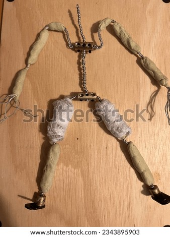 Close up of armature of human figure constructed with steel twisted wire for body arms and legs and metal bolts with animation hardening clay bones between joints built for stop motion video flat lay 