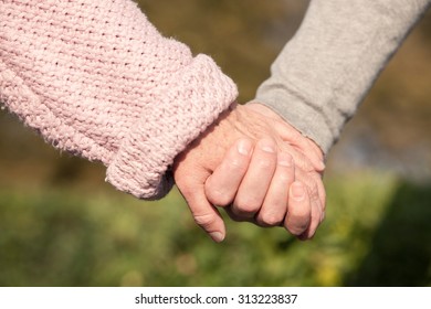 Close Up Of Arms Of Pretty Old Married Couple Holding Hands With Gentleness. The Man And Woman Are Dating In The Nature