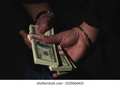 Close up arrested man holding money in handcuffs as a symbol of corruption, illegal gratuities. Copy space. Selective focuus on fingers and money. Horizontal image. - Shutterstock ID 2235066431