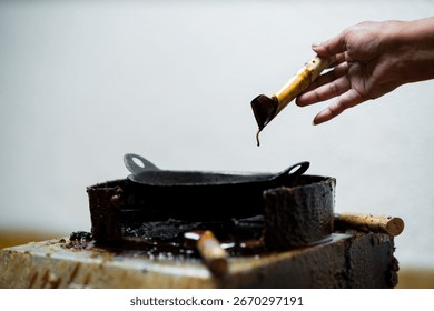 Close up of artisan hands using canting tool filled with hot wax to draw patterns on fabric, traditional Indonesian batik making process with smoke rising from the tool.