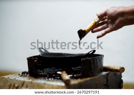 Close up of artisan hands using canting tool filled with hot wax to draw patterns on fabric, traditional Indonesian batik making process with smoke rising from the tool.