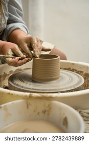 Close up of an artisan using a metal scraper to trim the rim of a spinning wet clay vessel