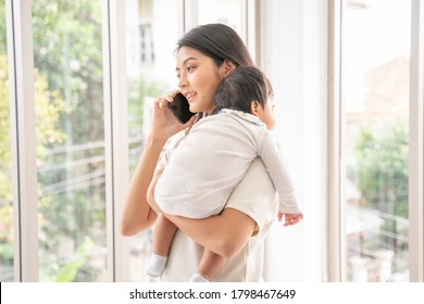 Close Up Of Asian Beautiful Mom Hugging Sleeping Newborn Baby In Her Arm And Kissing The Kid.Asian Mother Look Out The Window And Holding Her Baby Head In Home.she Is Happy To Stay At Home With Baby.