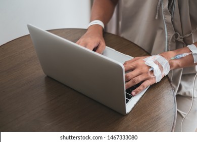 Close Up Asian Business Man Working On Laptop Though Hospital Internet During Recovery State On Wood Table Along Patient Bed While Getting Infusion. Always Working Concept.