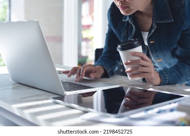 Close Up Of Asian Casual Business Woman Working On Laptop Computer, Hand Holding Cup Of Coffee With Digital Tablet On Desk At Home, Working From Home, Casual Business, Telecommuting Concept