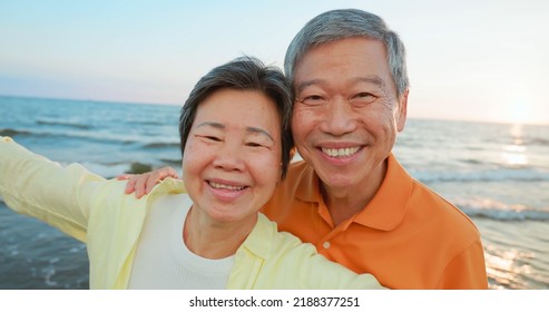 close up of asian elderly carefree couple standing on the beach and smiling at you happily in sunset background - Powered by Shutterstock