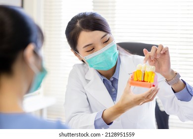 Close Up Of Asian Female Dentist Introduces Patient For Dental Implant By Denture Model While They Wear Protective Face Mask To Prevent COVID19