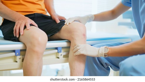 Close Up Of Asian Female Doctor Wearing Face Mask Is Examiniting Senior Elder Man Patient Knee Joint With Hands And Asking Him About Pain Symptom In Hospital 