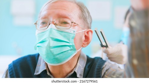 Close Up Of Asian Female Doctor Wearing Face Mask Is Using Tuning Fork For Hearing Tests To Elder Senior Man Patient In Hospital