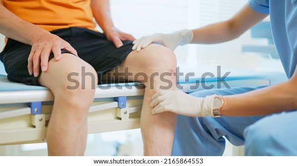 close up of asian female doctor\
wearing face mask is examiniting senior elder man patient knee\
joint with hands and asking him about pain symptom in hospital\
