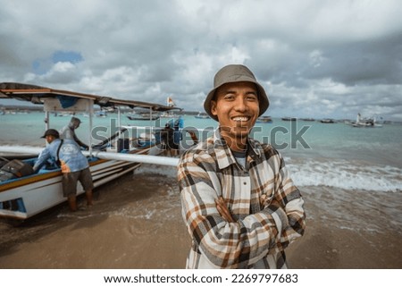 close up of Asian fisherman smiling with crossed hands against the background of a small boat leaning on the beach