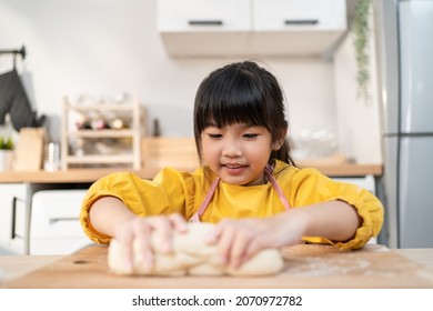 Close up Asian happy young kid girl doing homemade bakery in kitchen. Adorable little child sit on table feeling happy and enjoy learn to cooking foods or baking  kneads yeast dough with hands at home