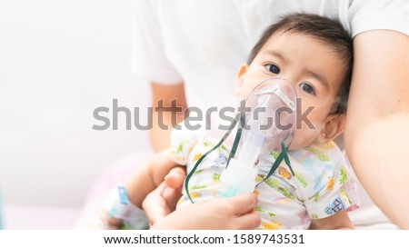 Close up of asian little baby boy is treated respiratory problem with vapor nebulizer to relief cough symptom in the hospital room , concept of pediatric patient care for sick in the hospital.