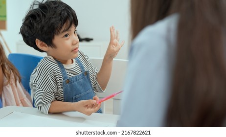 Close Up Asian Little Boy Doing Maths On White Table While Asian Female Teacher Teach Sit On The Chair In Classroom At Kindergarten.Financial Literacy Course For Children Of Preschool And School Age.