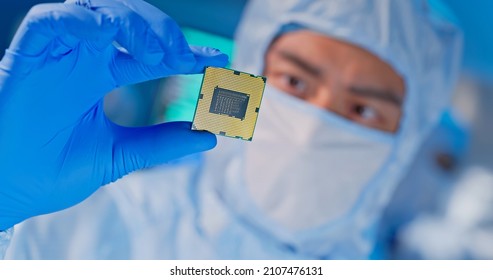 Close Up Of Asian Male Design Engineer In Sterile Coverall Holds Microchip With Gloves And Examines It - Ultra Modern Electronic Manufacturing Factory