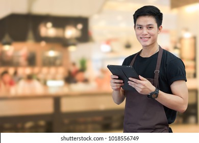 Close Up Asian Man Barista Holding Tablet For Checking Order From Customer On Blurred Coffee Cafe Shop Background , SME Business Concept