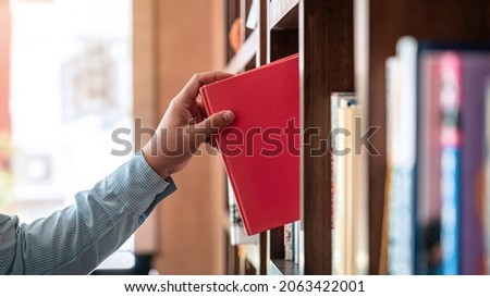Close up of asian man checking interesting book from bookcase to searching a book and taking off book from the bookshelf in library while reading a book to relaxation from work hard